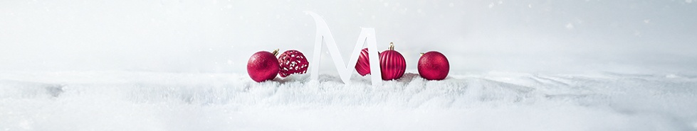 W centrum biała litera M, wokół bombki w kolorze wiśniowym. Białe tło ze światełkami łączy się z białym podłożem w postaci śniegu.