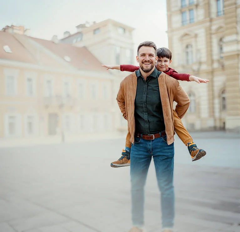soba stoi na miejskim placu przed zabytkowymi budynkami, niosąc dziecko na plecach. W prawym górnym rogu znajduje się różowe oznaczenie z napisem „DO 1000 ZŁ”.